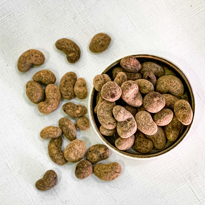 Choco covered cocoa beans, layered with dark, milk, and white chocolate, in a bowl on a white background.