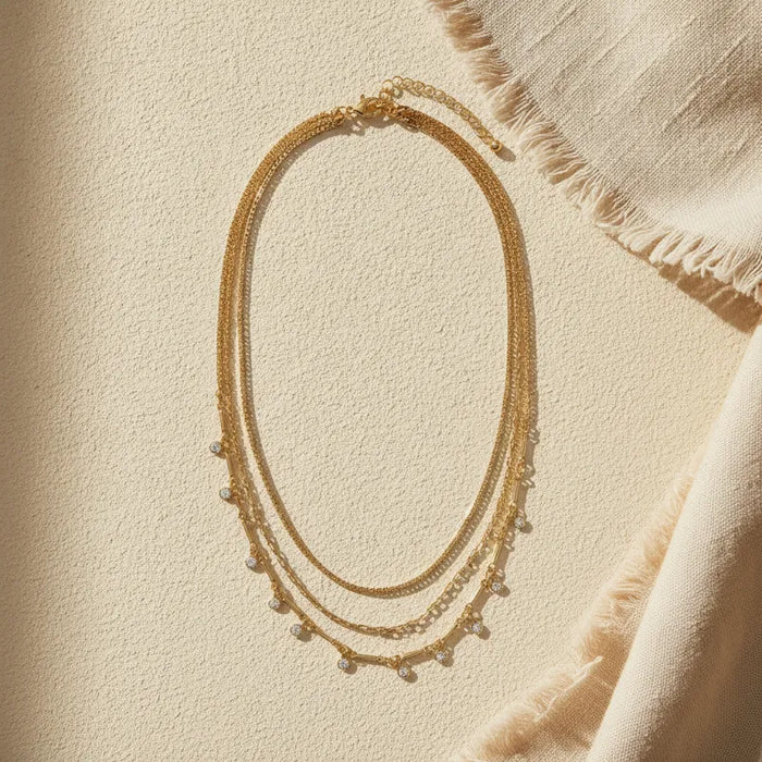 Gold layered necklace with delicate chain links and small pearl-like beads featuring shimmering crystal charms