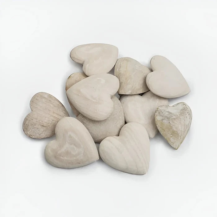Carved wooden heart surrounded by a pile of white pebbles on a white background