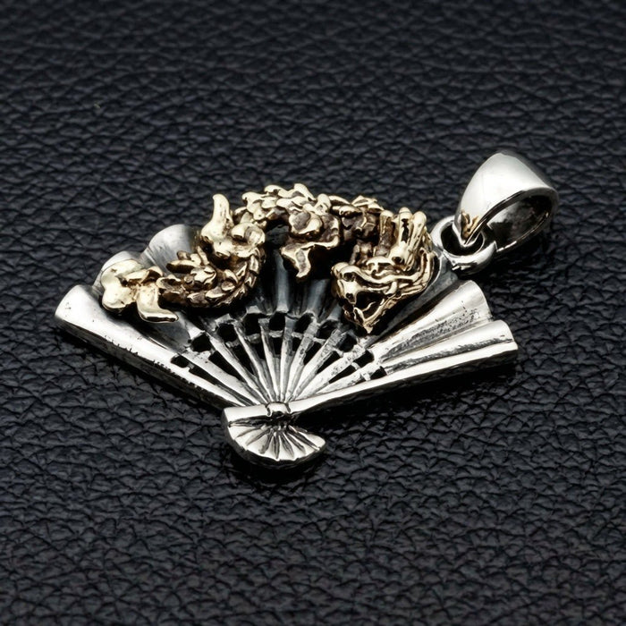 Three-quarter perspective of folding fan pendant showing sterling silver pleated ribs beneath coiling brass dragon motif