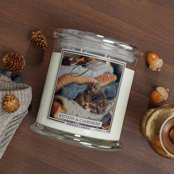 Kringle Candle jar with a kitten and cashmere 4-wick candle with cat label on a wooden surface with decorative elements.