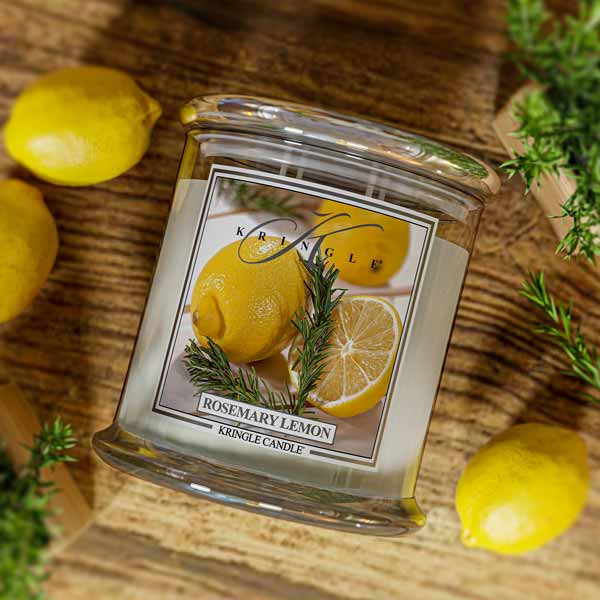 Lit Kringle Candle 4-wick in Rosemary Lemon scent on a wood background and label showing lemons and rosemary.