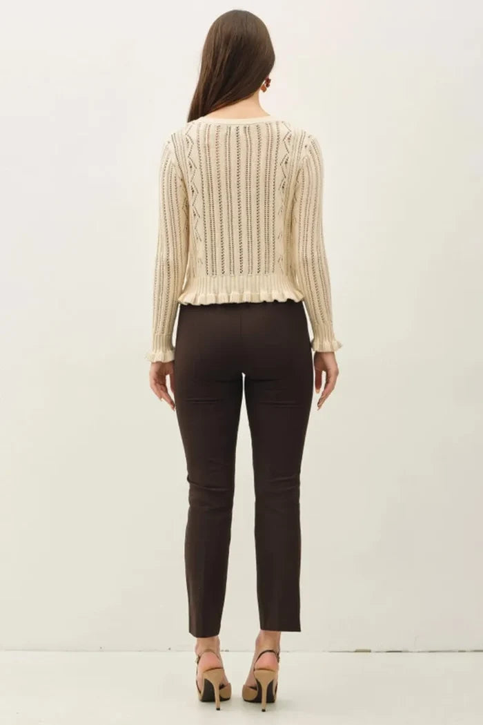 Cream-colored long-sleeved knitted ruffled pointelle crop cardigan with vertical ribbed texture and ruffled hem