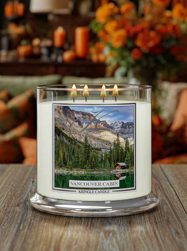 Four-wick candle lit, featuring a scenic label of a lakeside cabin surrounded by trees and mountains, "Vancouver Cabin"