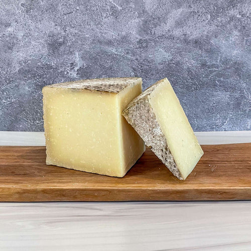 1605 Manchego cheese with natural rind on wooden board, sourced by Essex St. Cheese.