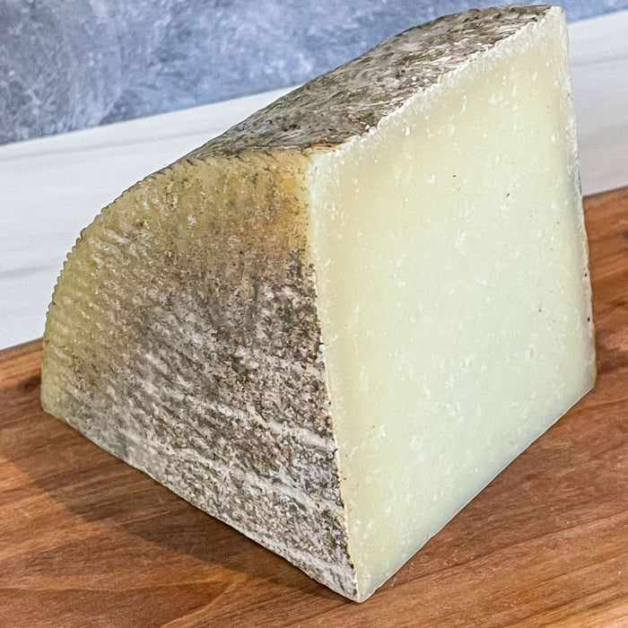 1605 Manchego cheese with unwaxed natural rind on a wooden board.