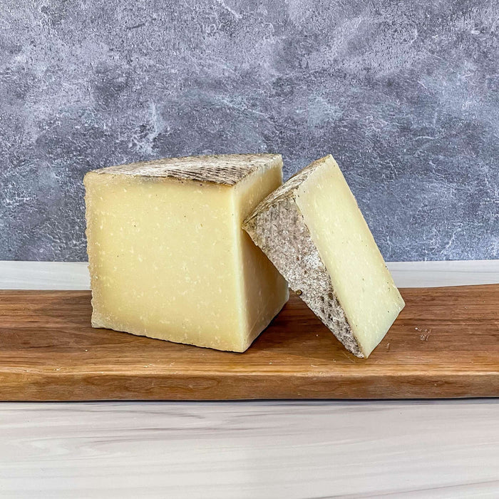 1605 Manchego cheese by Essex St. Cheese on wooden board, featuring a natural rind and rich texture.