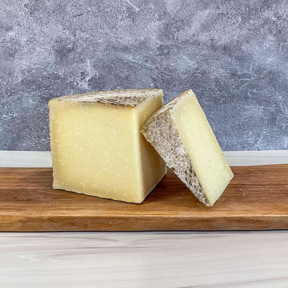 1605 Manchego cheese by Essex St. Cheese on wooden board, featuring a natural rind and rich texture.