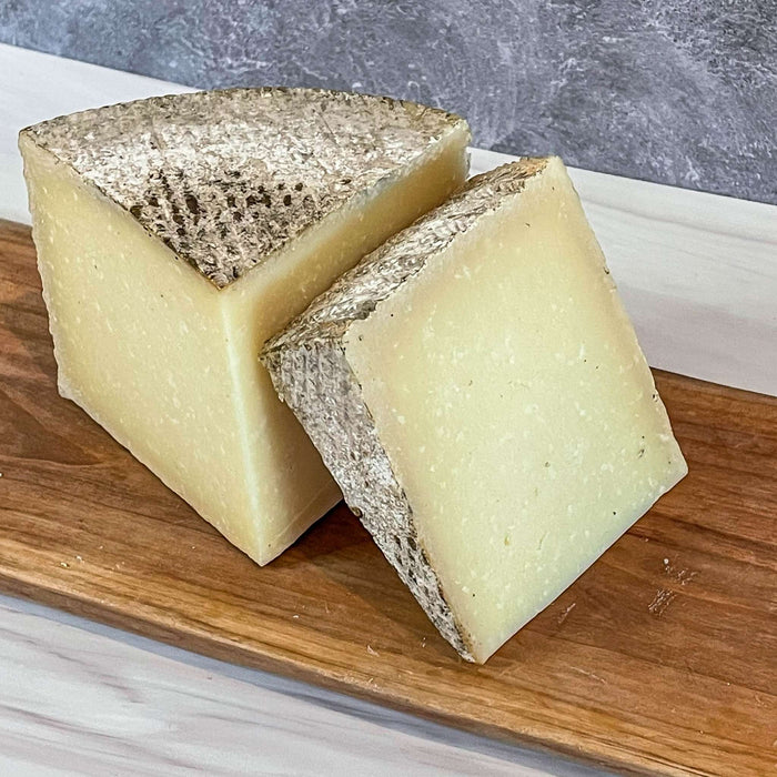 1605 Manchego cheese with unwaxed rind on a wooden board.