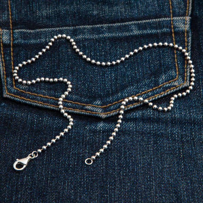 A 3mm sterling silver ball chain necklace laid out on dark denim.