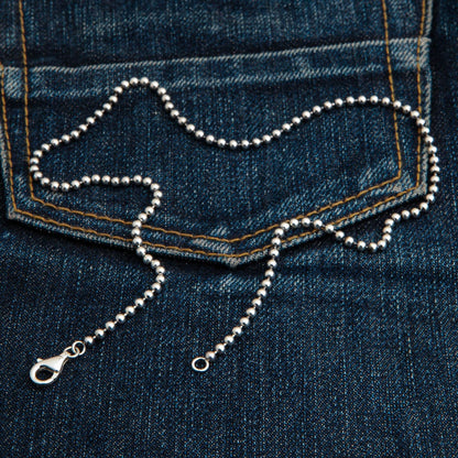 A 3mm sterling silver ball chain necklace laid out on dark denim.