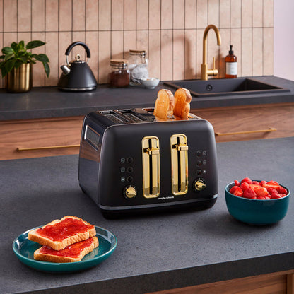 Black toaster with gold accents on a kitchen counter, surrounded by toast and fruit.