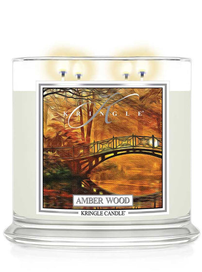 Kringle Candle lit 4-wick in Amber Wood scent with a scenic label on a white background