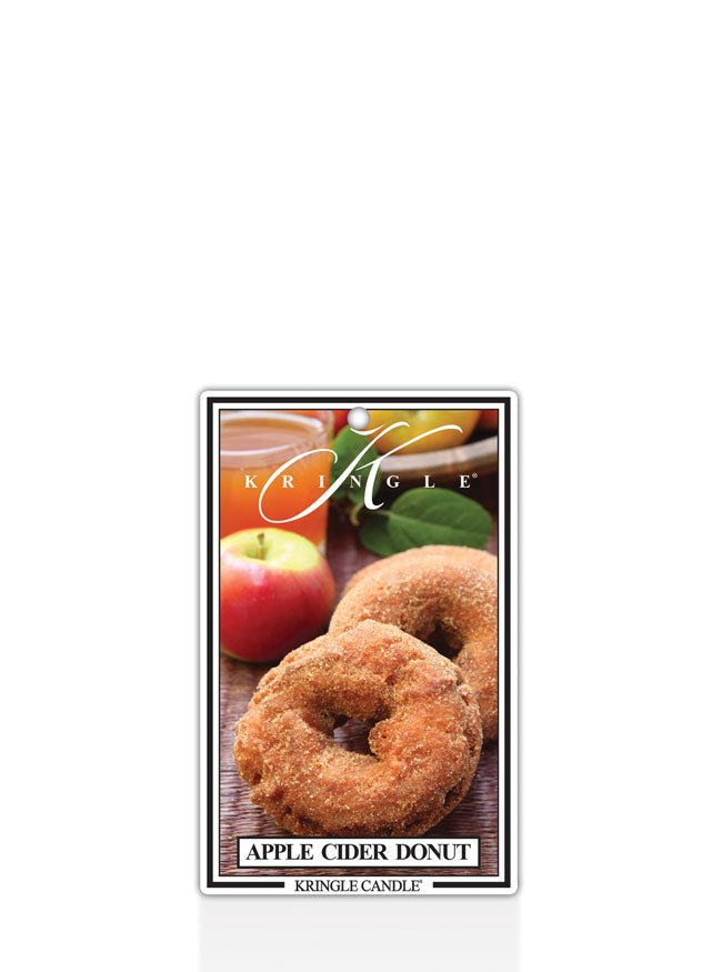 Kringle Candle Apple Cider Donut air freshener, designed for use in cars or small spaces. The packaging features two cinnamon-sugar-coated apple cider donuts on a wooden surface, with a fresh apple and a glass of apple cider in the background. The Kringle Candle logo is displayed at the top, with the scent name ‘Apple Cider Donut’ printed below.