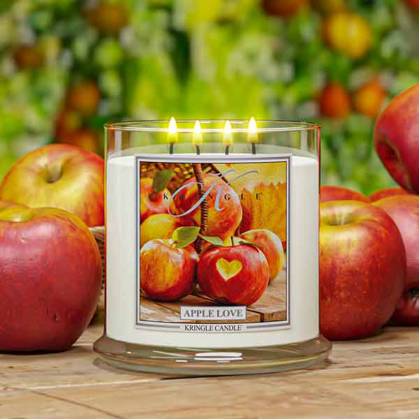 Kringle Candle with 4-wick candle 'Apple Love' design surrounded by apples on a wooden surface