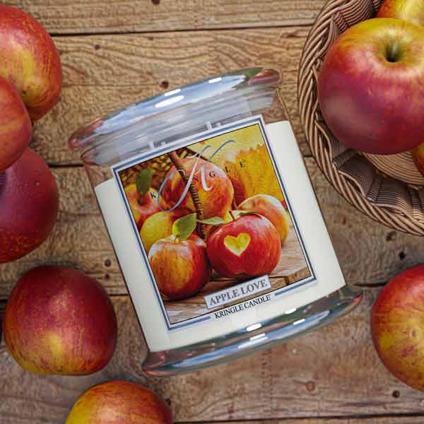 4-wick Applr Love Scented Candle with apple design on lid surrounded by apples on wooden surface