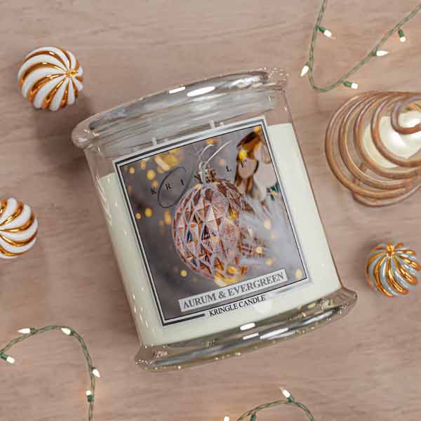 Kringle Candle  Aurum & Evergreen jar with decorative holiday ornament label of lights and ornaments on a wooden surface