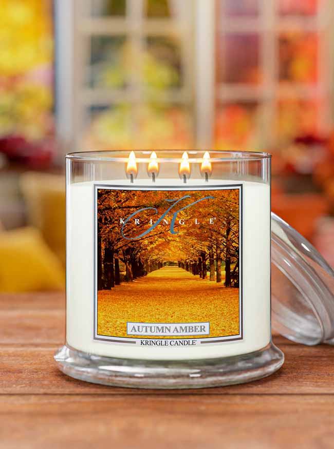 Kringle Candle with 'Autumn Amber' label on a wooden surface with blurred autumn-themed background