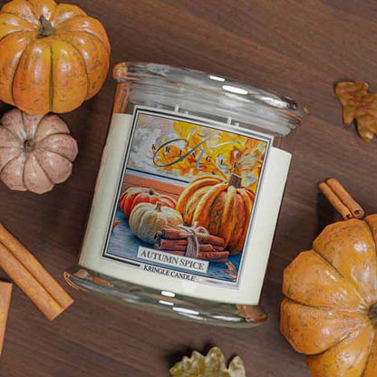 Kringle Candle Autumn Spice scented 4-wick candle with pumpkins and cinnamon sticks on a wooden surface