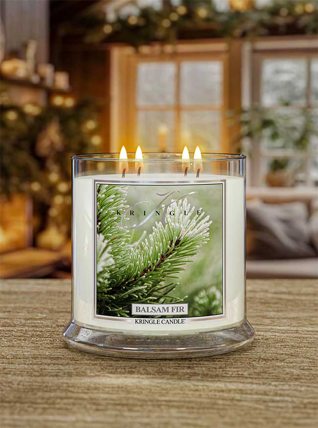 Kringle Candle Balsam Fir 4-wick lit candle on a wooden surface with a festive background