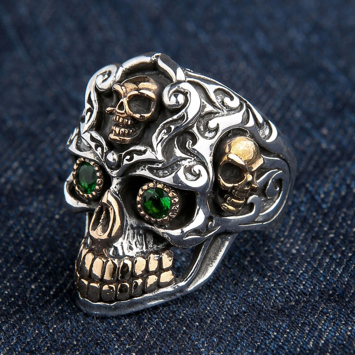 An angled view of the baroque skull ring, highlighting the side gold skulls and intricate scrollwork.