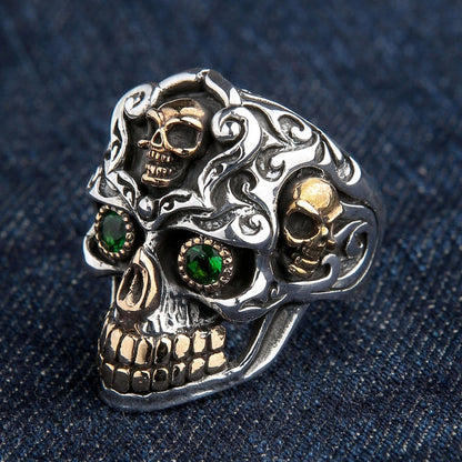 An angled view of the baroque skull ring, highlighting the side gold skulls and intricate scrollwork.