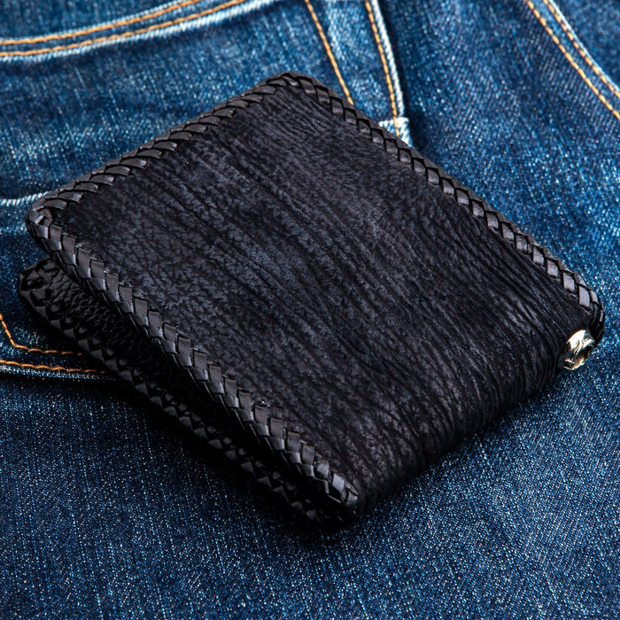 Three-quarter view on denim showing braided leather lacing around every edge of the stingray chain wallet.
