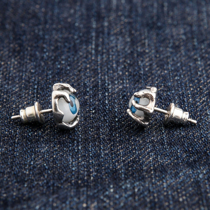 A pair of sterling silver monster claw earrings holding a realistic blue eye.