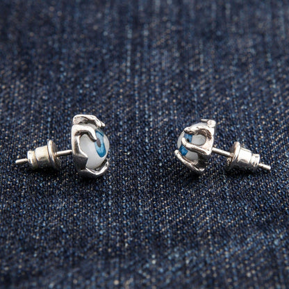 A pair of sterling silver monster claw earrings holding a realistic blue eye.