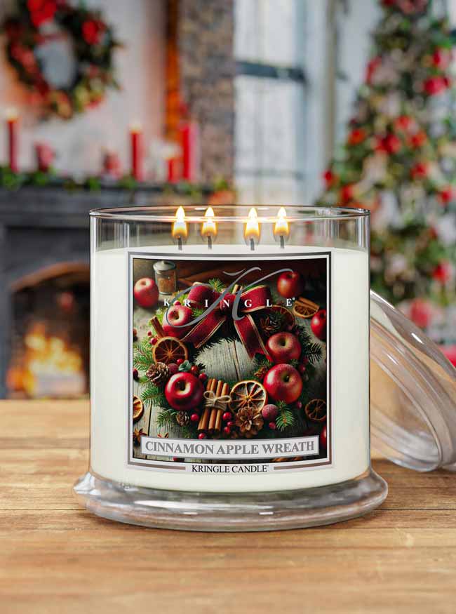 Kringle Candle with 'Cinnamon Apple Wreath' label on a wooden surface with Christmas decorations in the background.