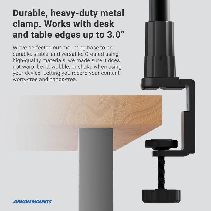 The Clamp Mounting Pedestal with 12 Gooseneck - Dual-T Compatible secures to the edge of a wooden table up to 3 inches thick, showcasing its durable black metal build and versatile mounting for devices.