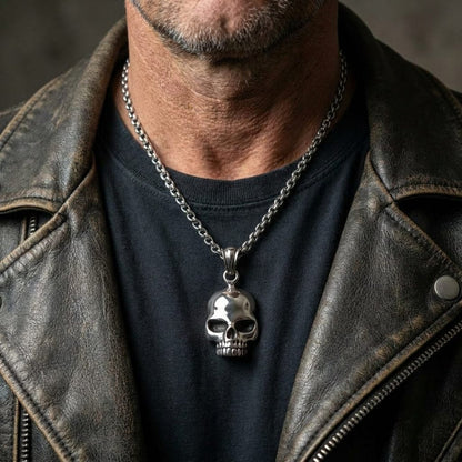 A man in a brown leather jacket wearing a polished silver biker skull pendant on a chain.