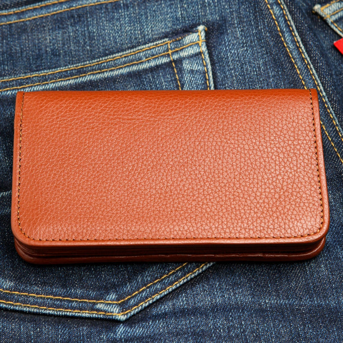 Pebble-grain cognac leather resting in a denim pocket, edge stitching running the full perimeter.