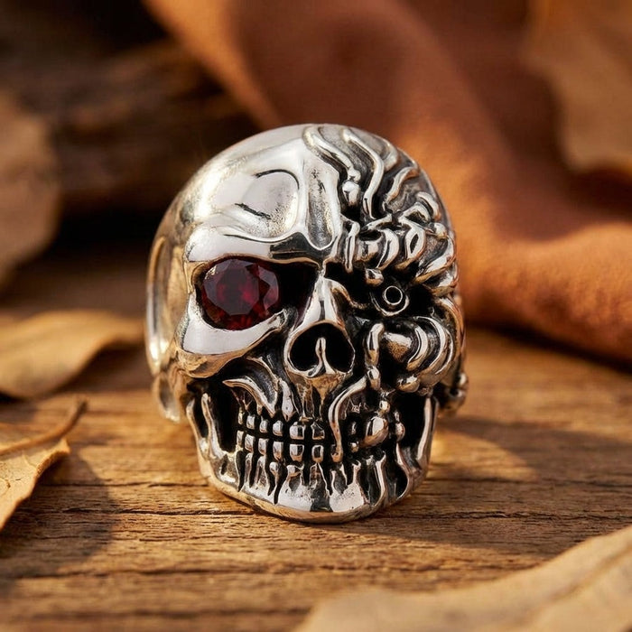 Cyborg terminator skull ring in sterling silver with red ruby eye displayed on wooden surface with autumn leaves
