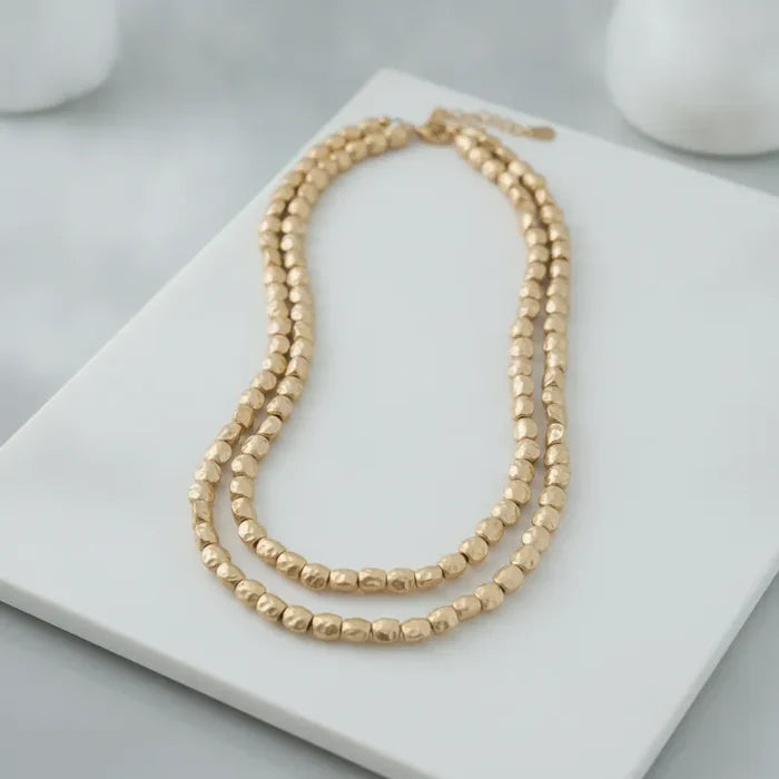 Double-strand matte gold hammered bead statement necklace with a textured hammered finish in gold tone