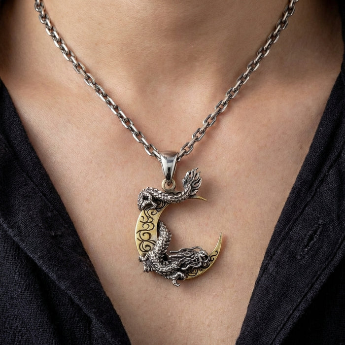 Sterling silver dragon wrapped around gold crescent moon pendant necklace with intricate detailing, worn on a silver chain against skin with dark v-neck clothing