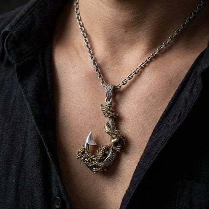 Sterling silver and gold dragon fish hook pendant necklace worn on a man's chest with an open dark shirt, featuring an intricately detailed dragon wrapped around a curved hook on a silver link chain