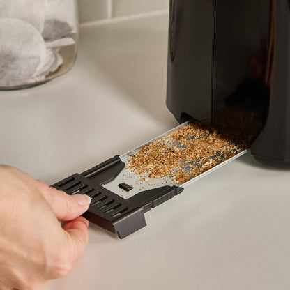 Person removing crumbs from a toaster crumb tray on a kitchen counter.