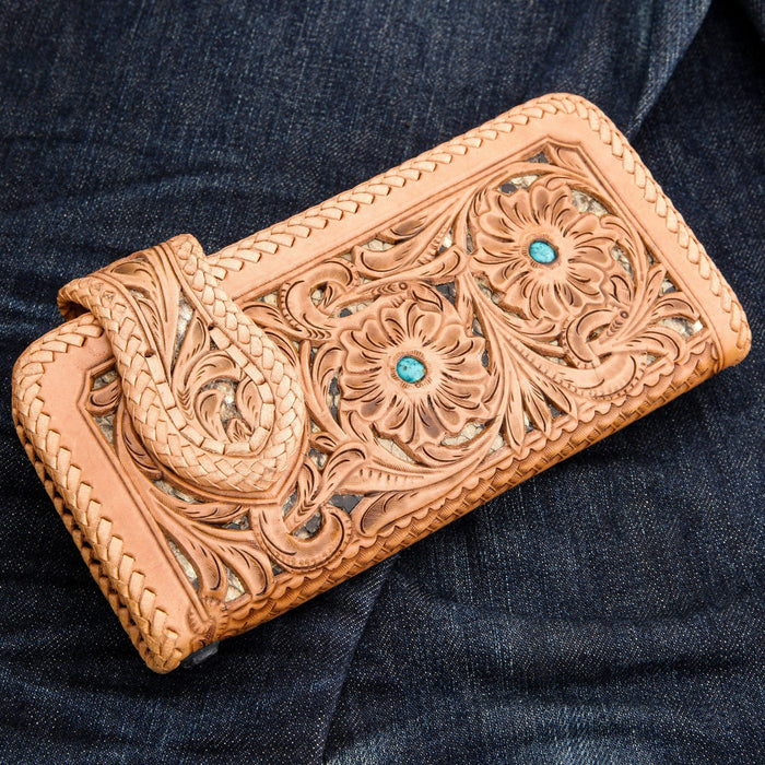 Light brown floral carved cowhide leather biker wallet with turquoise conchos and braided edges, resting on dark blue denim