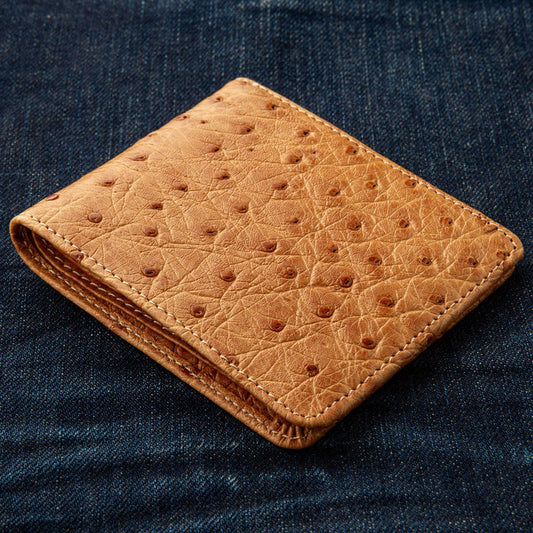 The closed tan ostrich wallet sitting on a pair of dark denim jeans.
