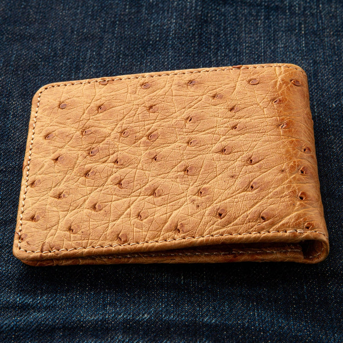 A shot of the men's tan ostrich wallet, closed, on a jeans background.