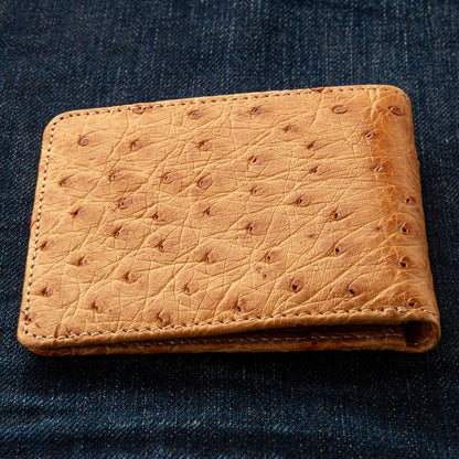 A shot of the men's tan ostrich wallet, closed, on a jeans background.