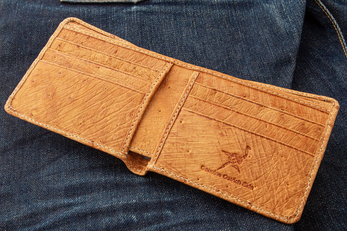 The genuine ostrich skin wallet in tan brown, laid open on denim, showing the interior card slots.