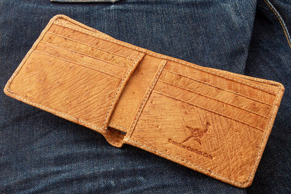 The genuine ostrich skin wallet in tan brown, laid open on denim, showing the interior card slots.