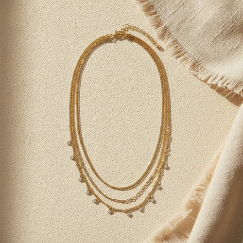 Gold layered necklace with delicate chain links and small pearl-like beads featuring shimmering crystal charms