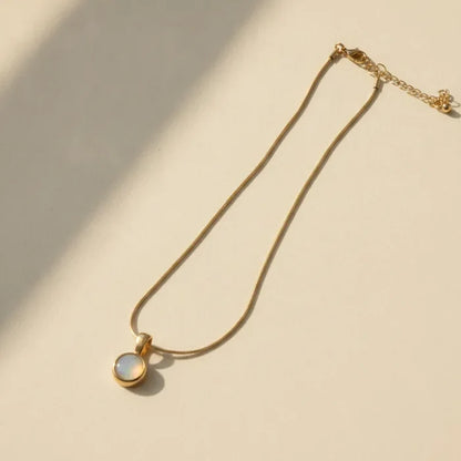 Gold snake chain necklace with round mother of pearl pendant featuring a soft iridescent sheen