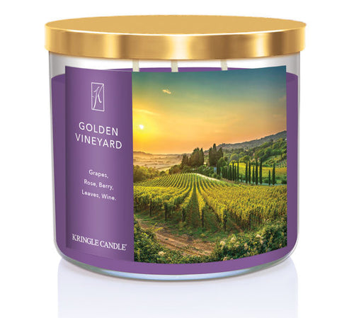 A three-wick candle in a clear glass jar with a gold lid and a scenic vineyard-themed label. The label features a picturesque vineyard at sunset with rolling green hills and a golden sky. The candle’s wax is deep purple, and the wicks are unlit. The scent notes listed are grapes, rose, berry, leaves, and wine.