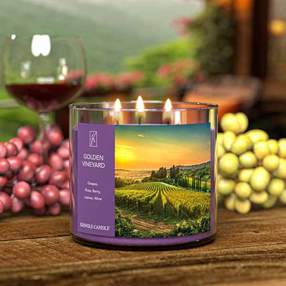 A three-wick lit candle in a clear glass jar with a scenic vineyard-themed label. The candle’s wax is deep purple, and all three wicks are burning.