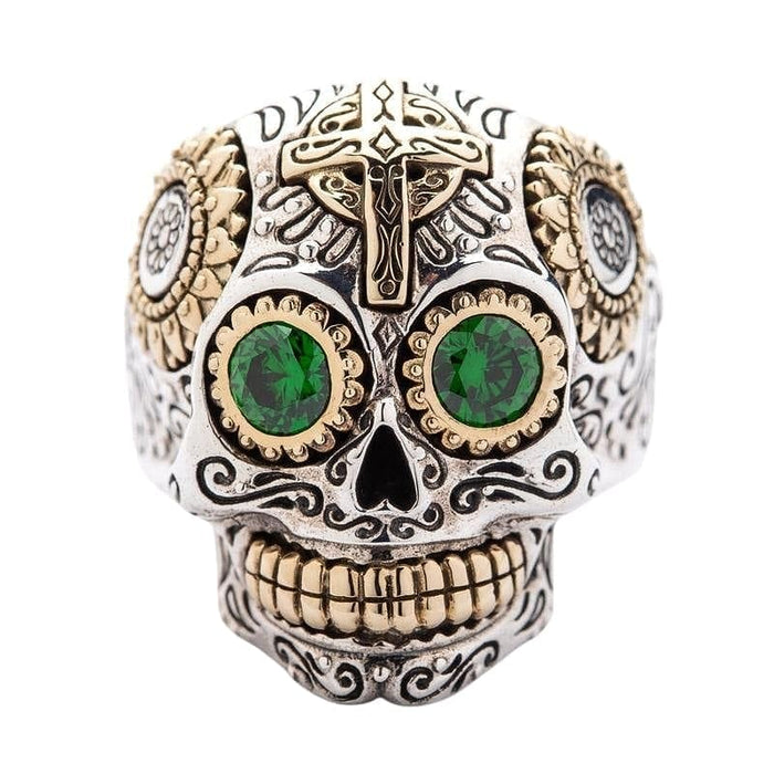 A sterling silver sugar skull ring with vibrant green CZ eyes and golden brass accents.