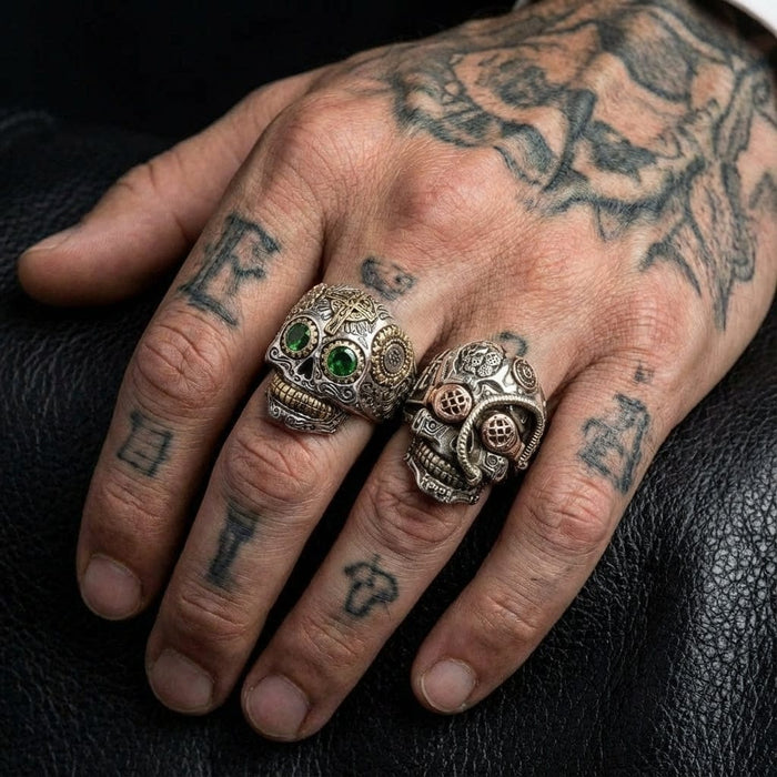 Sterling silver sugar skull ring featuring green gemstone eyes worn on a tattooed male hand, showcasing detailed biker jewelry design.